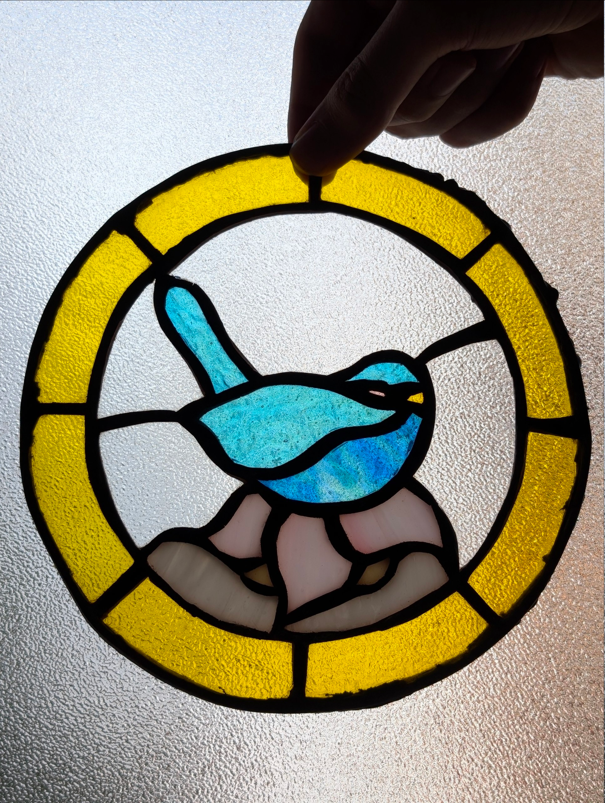 Vidriera circular con un pájaro azul, sujeta con la mano