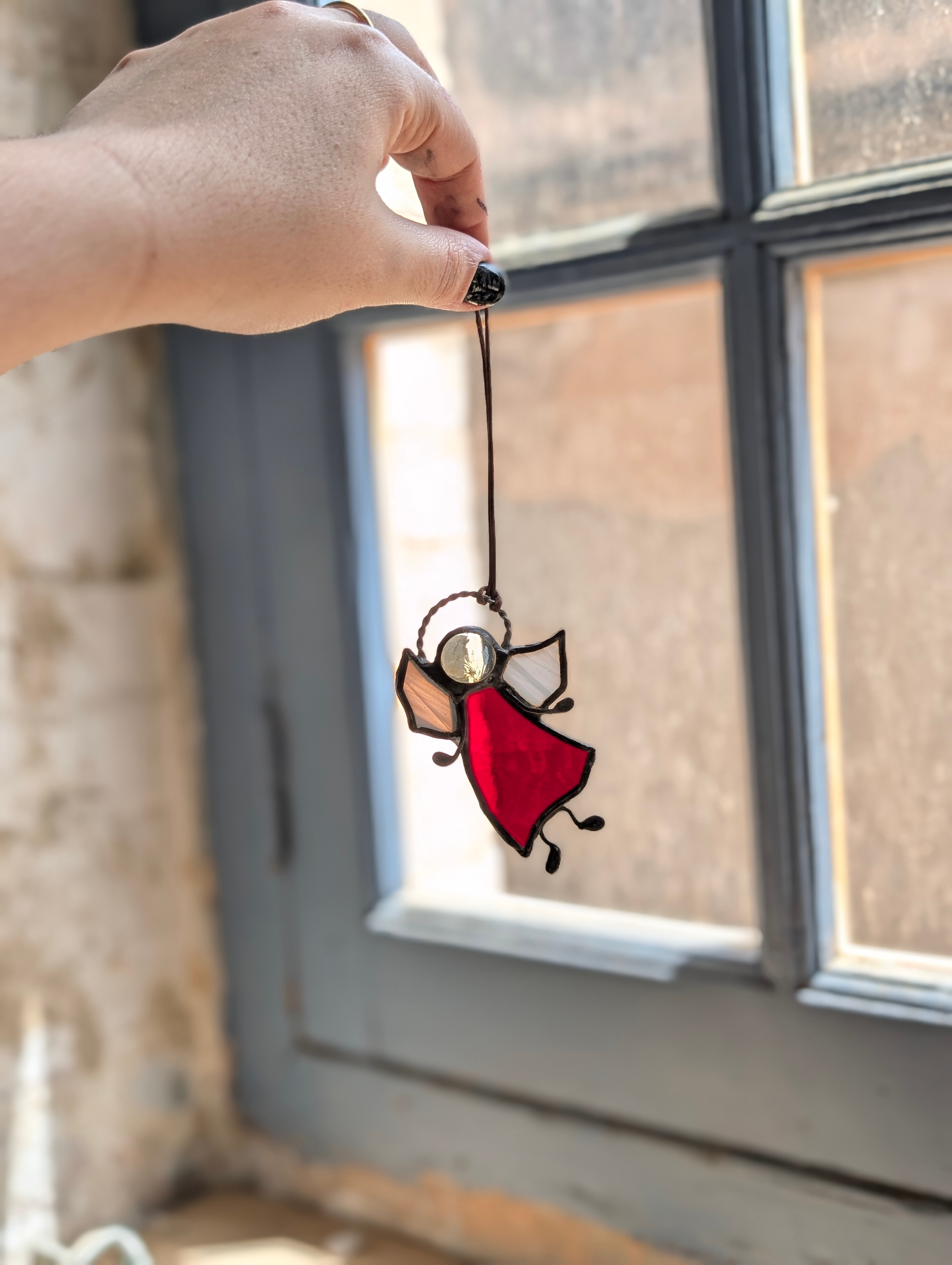 Figura de vidriera de un ángel con vestido rojo, sujeta con la mano