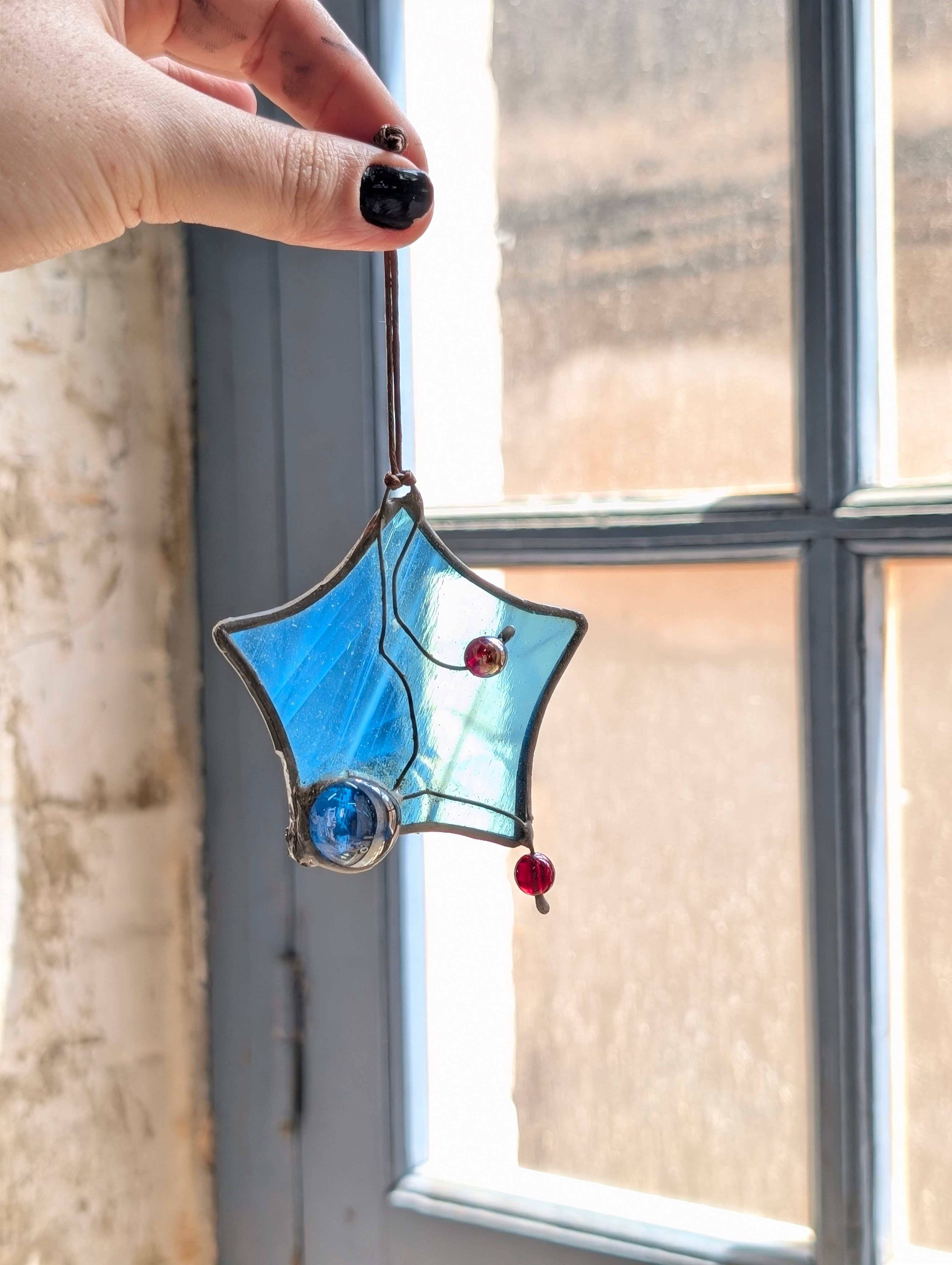 Adorno de vidriera en forma de estrella azul, sujeto con la mano junto a una ventana