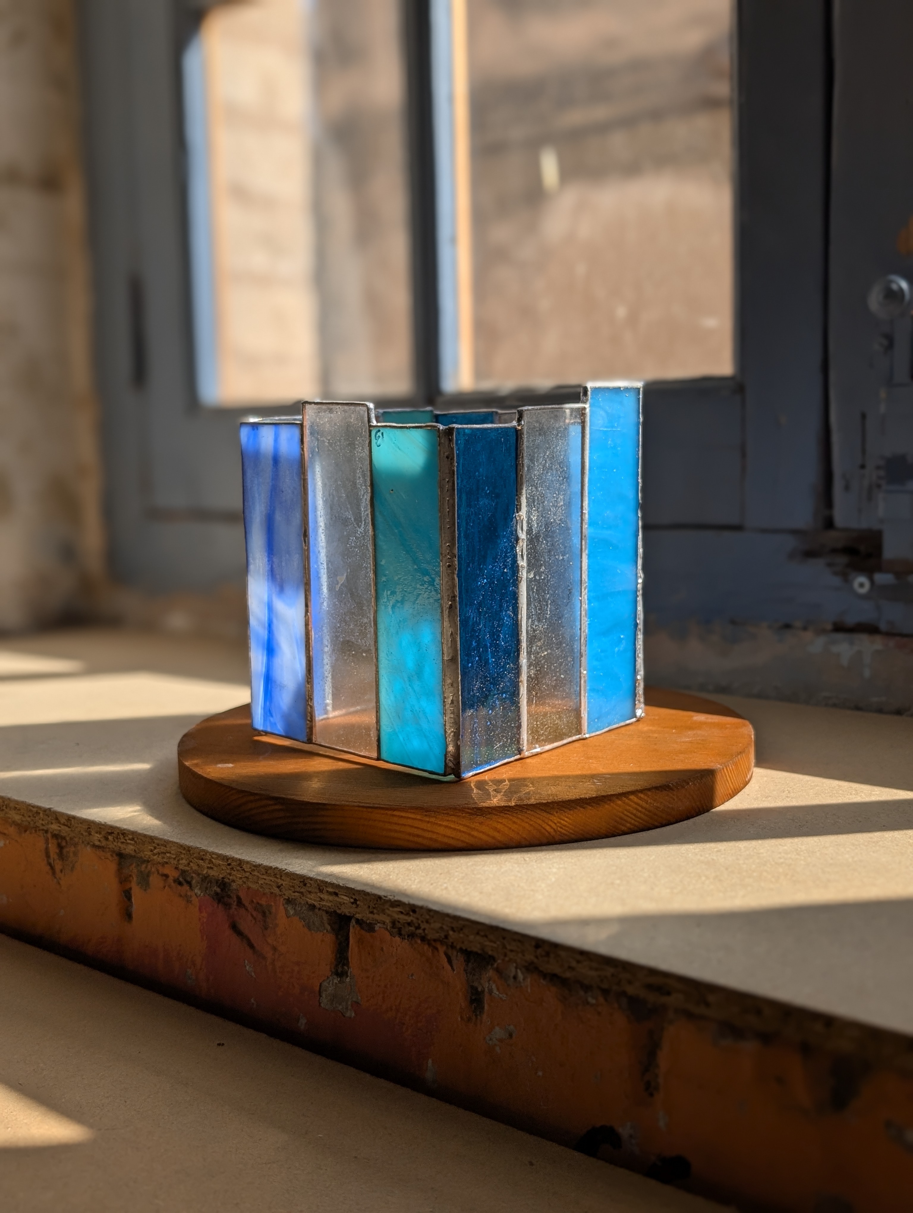 Portavelas de vidriera en tonos azules sobre una base de madera