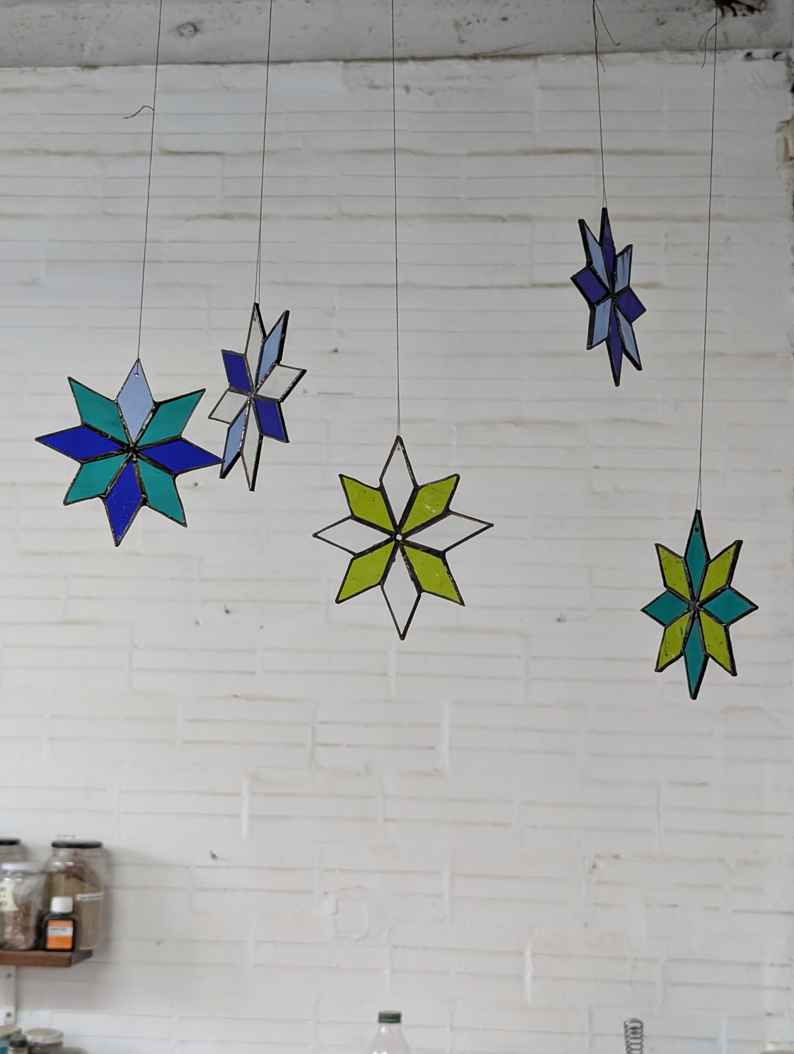 Cinco estrellas de vidriera colgadas contra una pared de ladrillo blanco