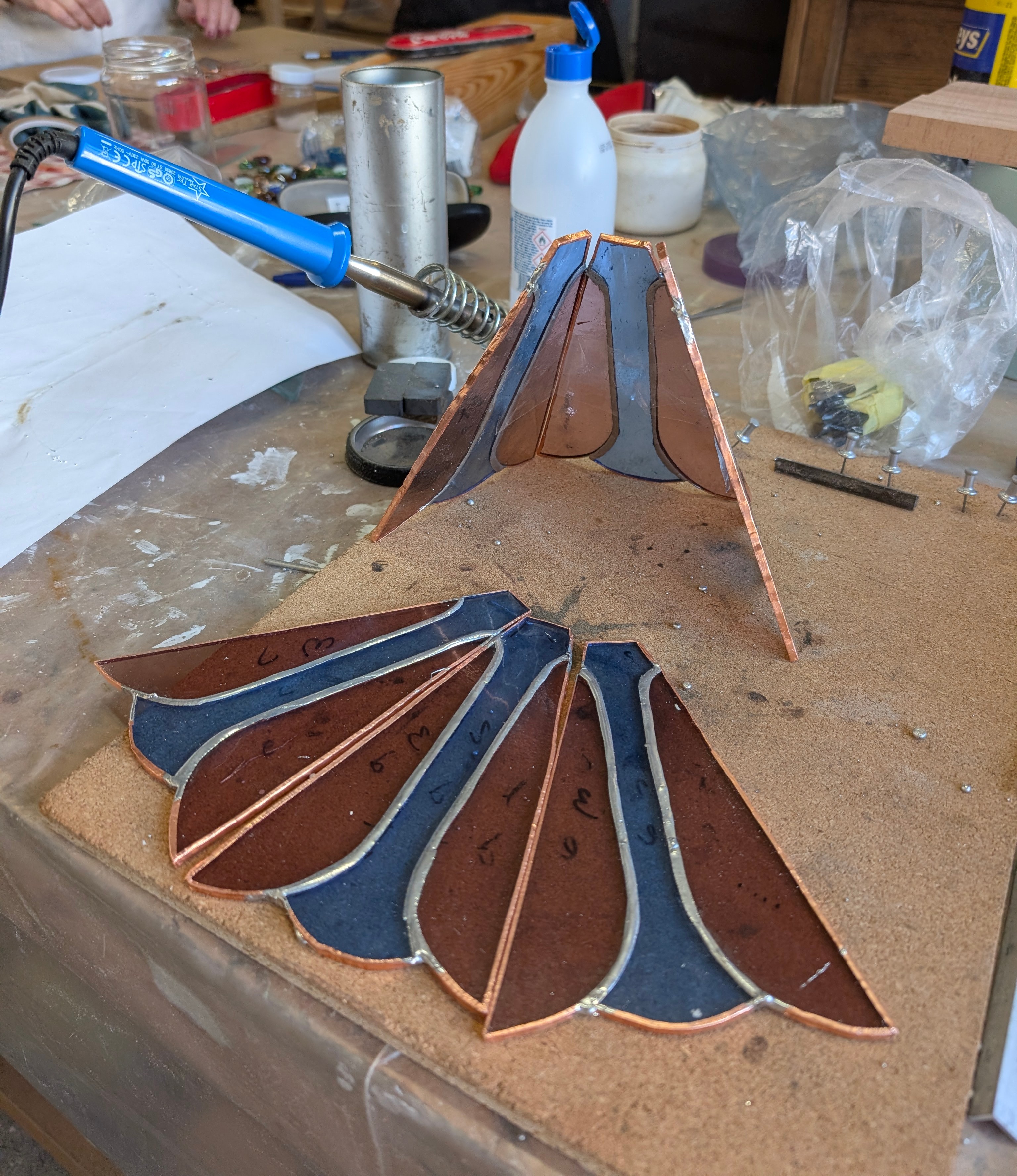 Piezas de vidrio emplomadas en forma de abanico para una pantalla de lámpara, en proceso de soldadura